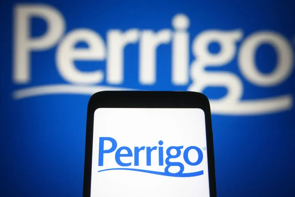 In this photo illustration a Perrigo Company logo of a pharmaceutical company is seen on a smartphone and a pc screen.