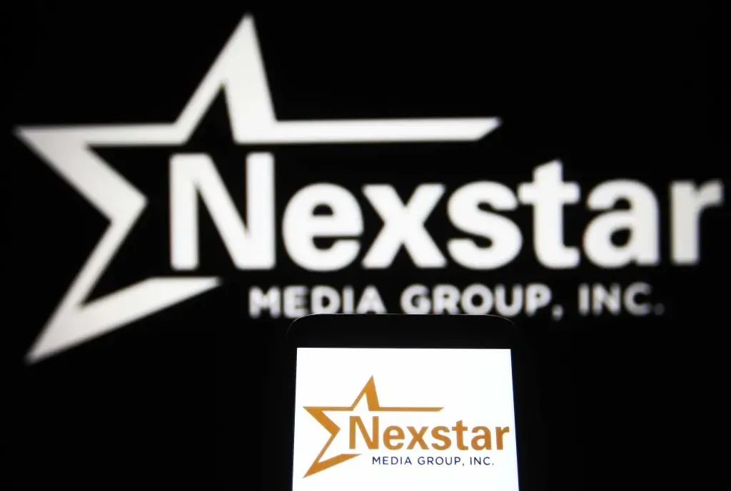 In this photo illustration, Nexstar Media Group, Inc. logo is seen on a smartphone and a pc screen.