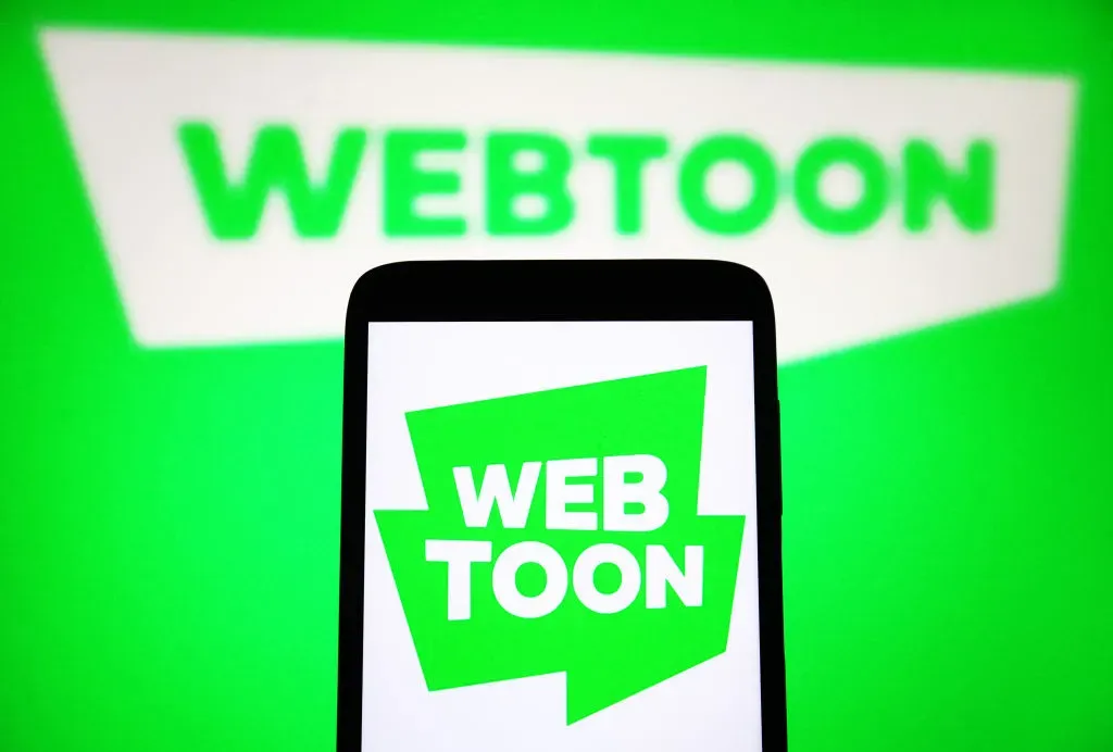 In this photo illustration, a Webtoon Entertainment Inc. logo is seen on a smartphone and on a pc screen. 
