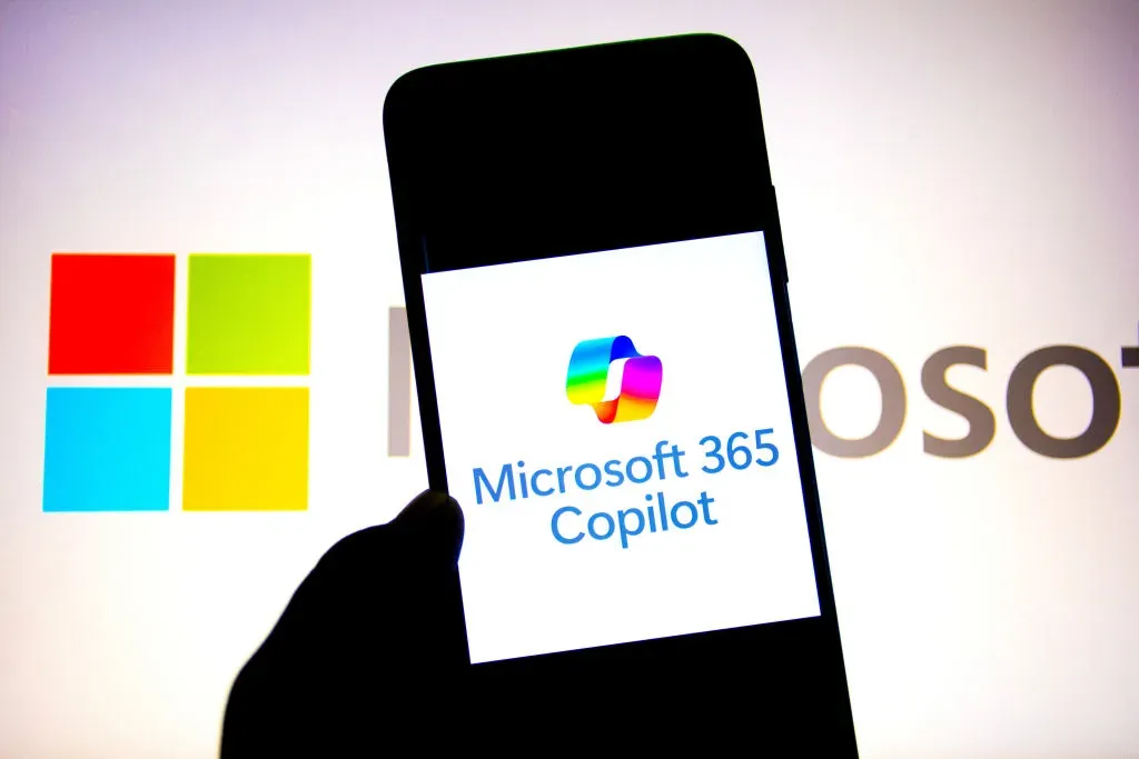 In this photo illustration, a Microsoft 365 Copilot logo seen displayed on a smartphone with a Microsoft Logo in the background. 