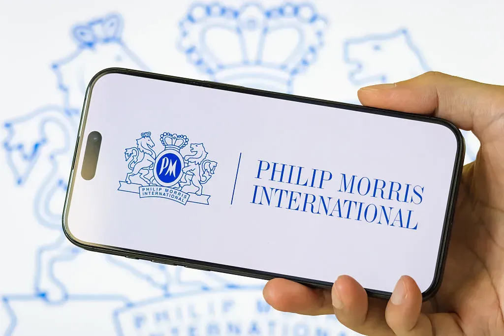 In this photo illustration, a person holds a smartphone displaying the logo of Philip Morris International Inc. 