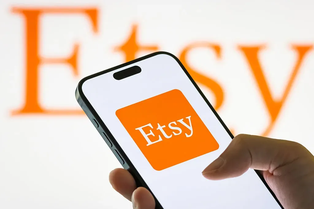 In this photo illustration, a person holds a smartphone displaying the logo of Etsy Inc.