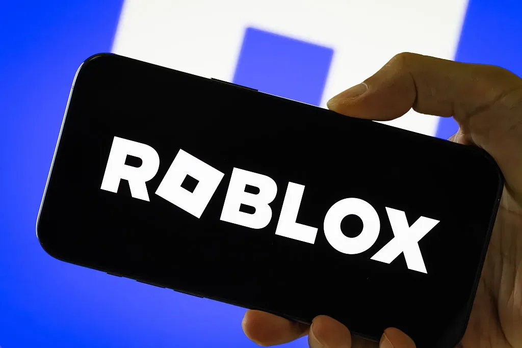  In this photo illustration, a person holds a smartphone displaying the logo of Roblox Corporation.