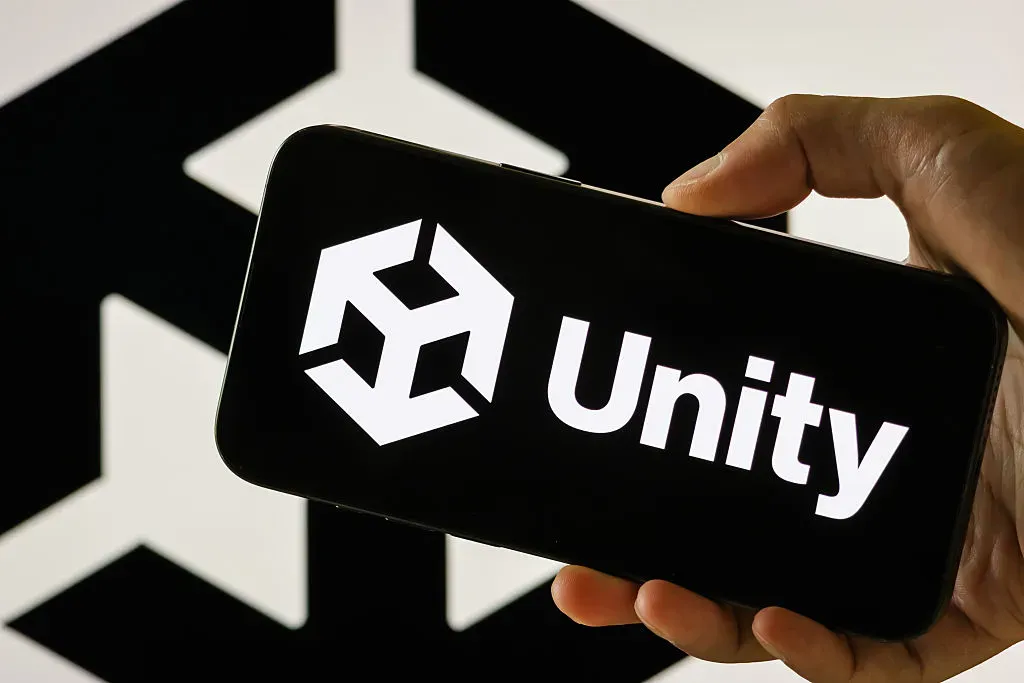 In this photo illustration, a person holds a smartphone displaying the logo of Unity Technologies.
