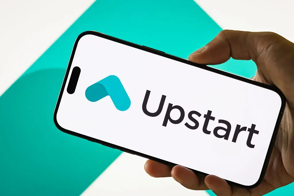  In this photo illustration, a person holds a smartphone displaying the logo of Upstart Holdings Inc.
