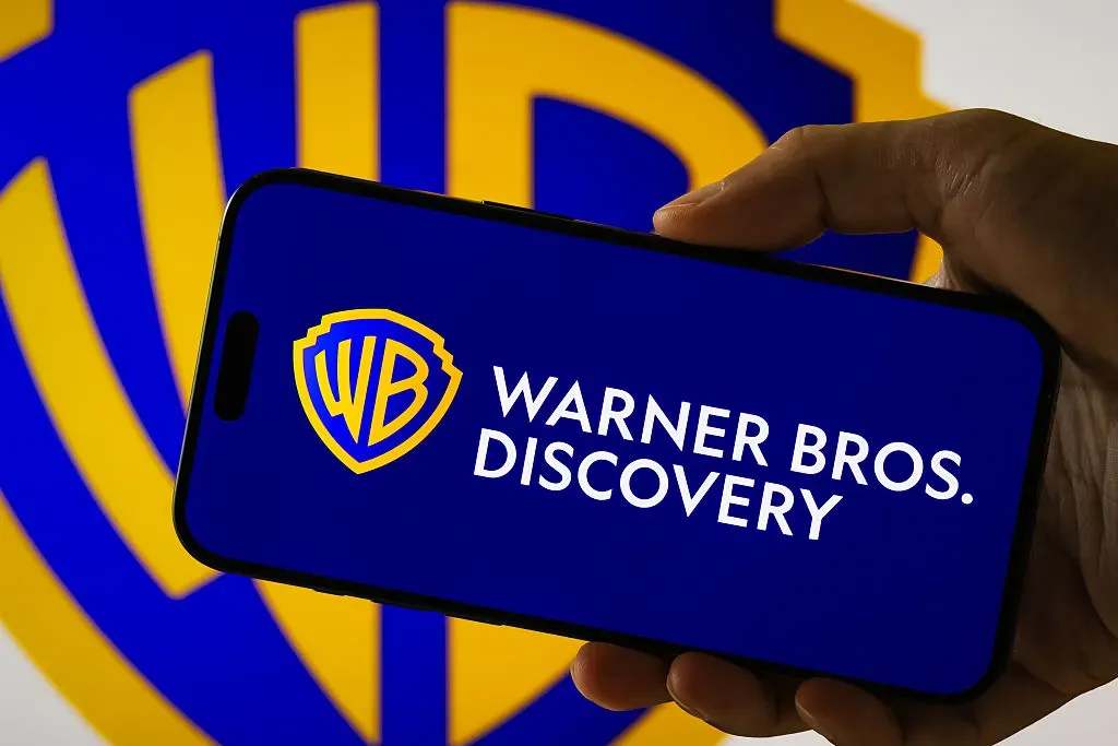 In this photo illustration, a person holds a smartphone displaying the logo of Warner Bros. Discovery Inc. 