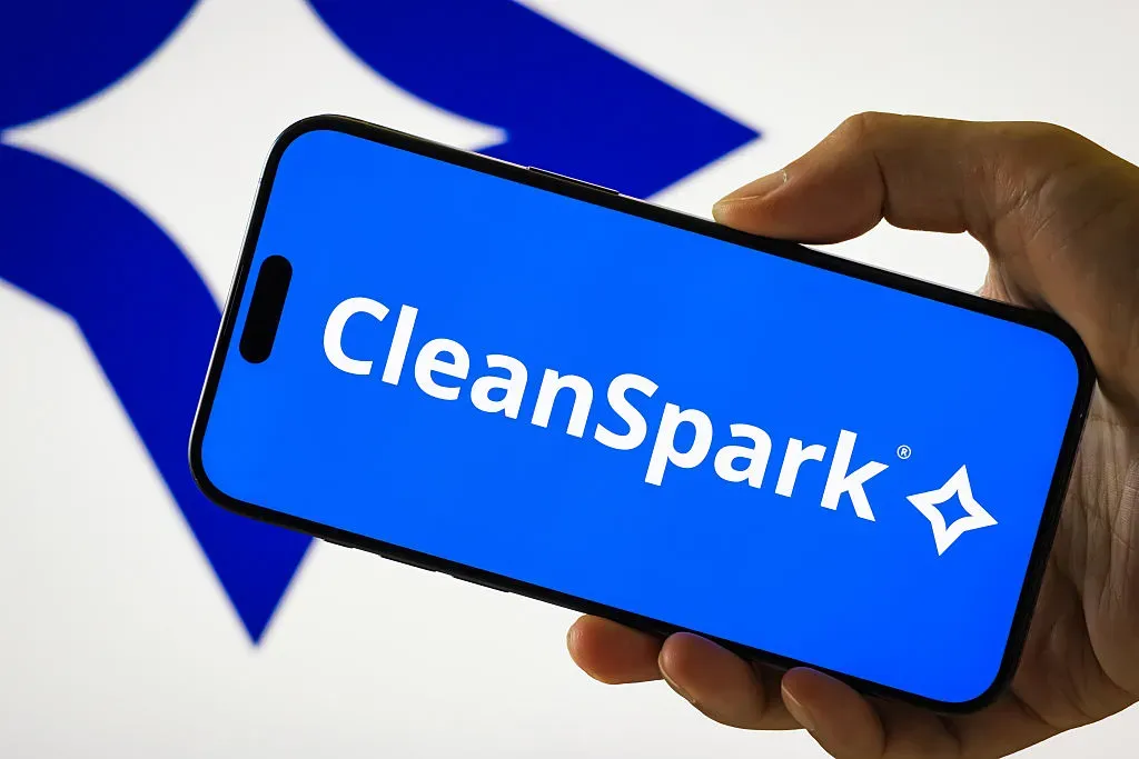 In this photo illustration, a person holds a smartphone displaying the logo of CleanSpark Inc.