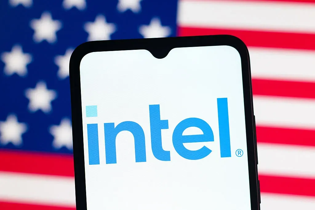  In this photo illustration, the Intel Corporation logo is seen displayed on a smartphone screen and the United States flag in the background.