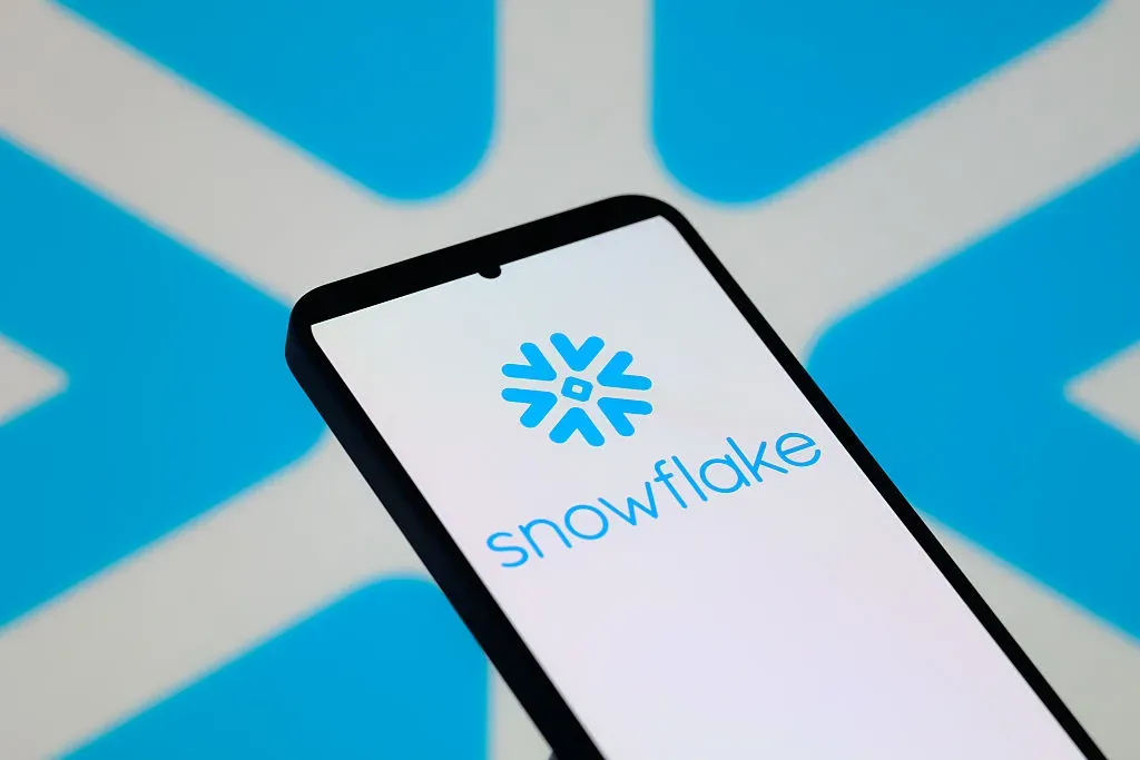 The Snowflake Ink logo is displayed on a mobile phone with the company's emblem seen in the background.