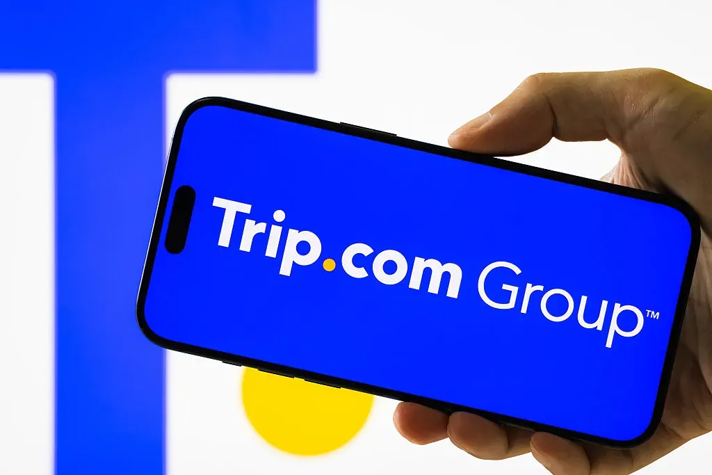 In this photo illustration, a hand holds a smartphone displaying the logo of Trip.com Group Limited.