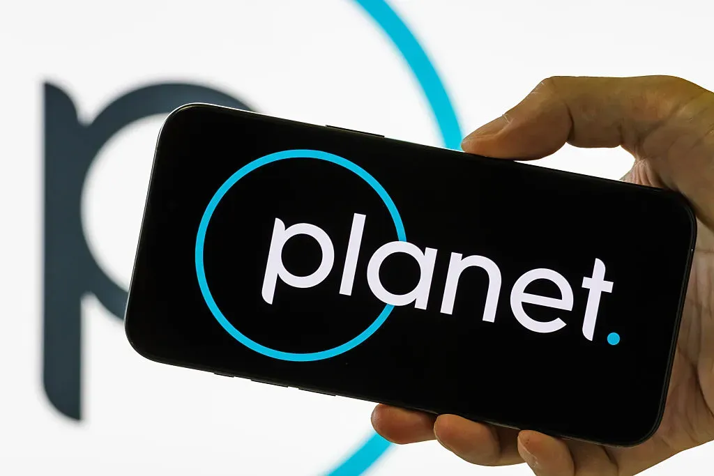 In this photo illustration, a smartphone held in a hand shows the logo of Planet Labs PBC