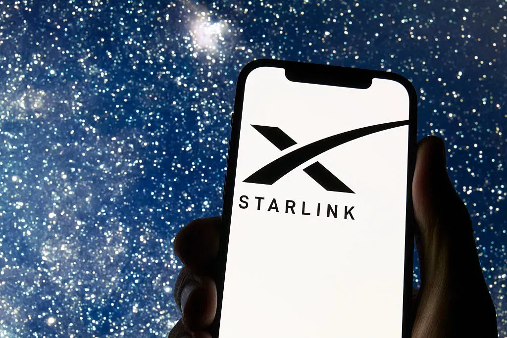 The Starlink logo appears on a smartphone screen with a starry night sky in the background.