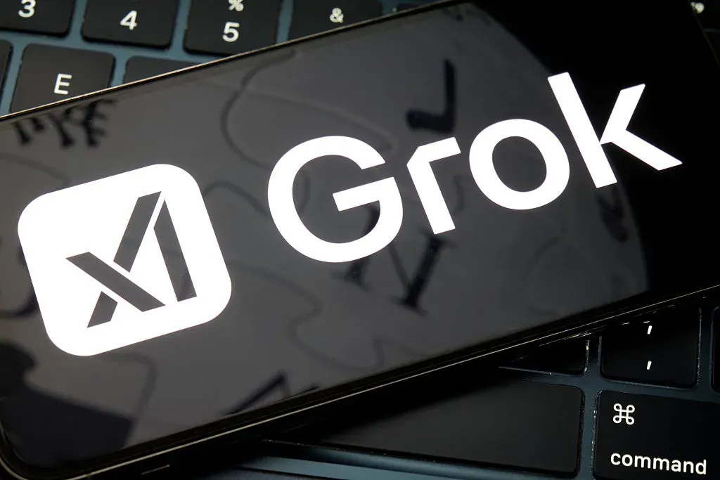 A smartphone displays the Grok logo while resting on a computer keyboard.