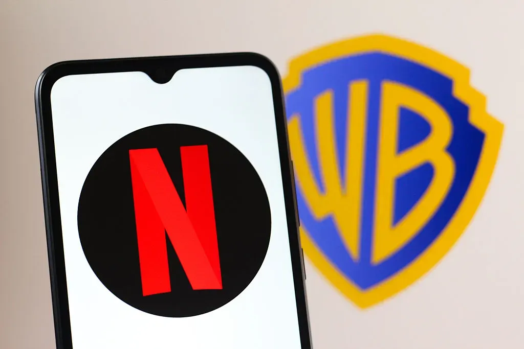 In this photo illustration, the Netflix logo is seen displayed on a smartphone screen and a Warner Bros. Discovery logo in the background.