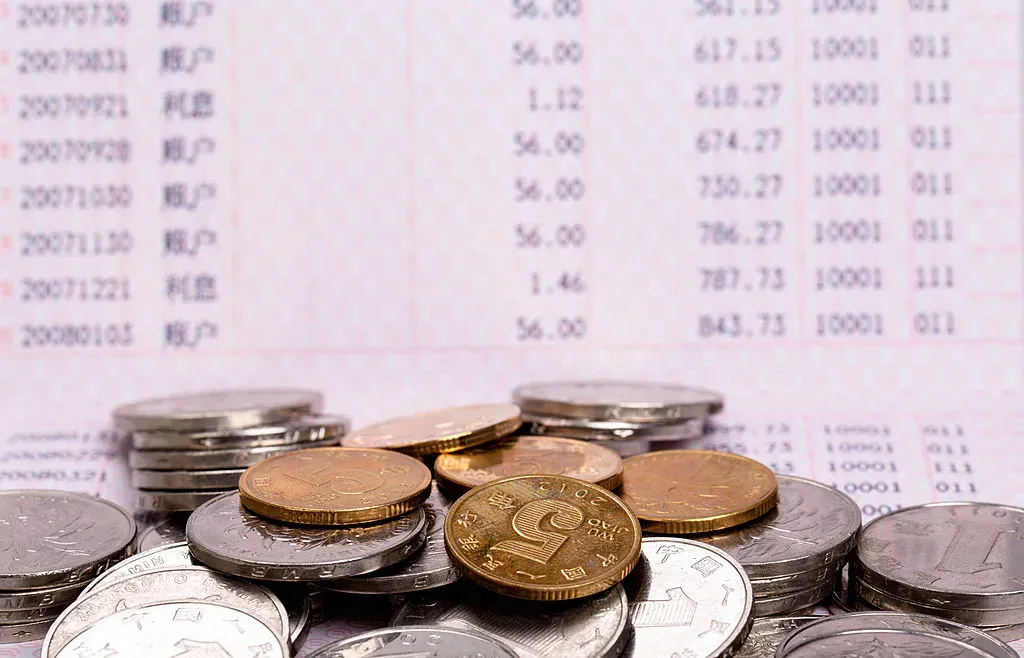 Chinese RMB coins are arranged in front of a passbook for a photograph. 