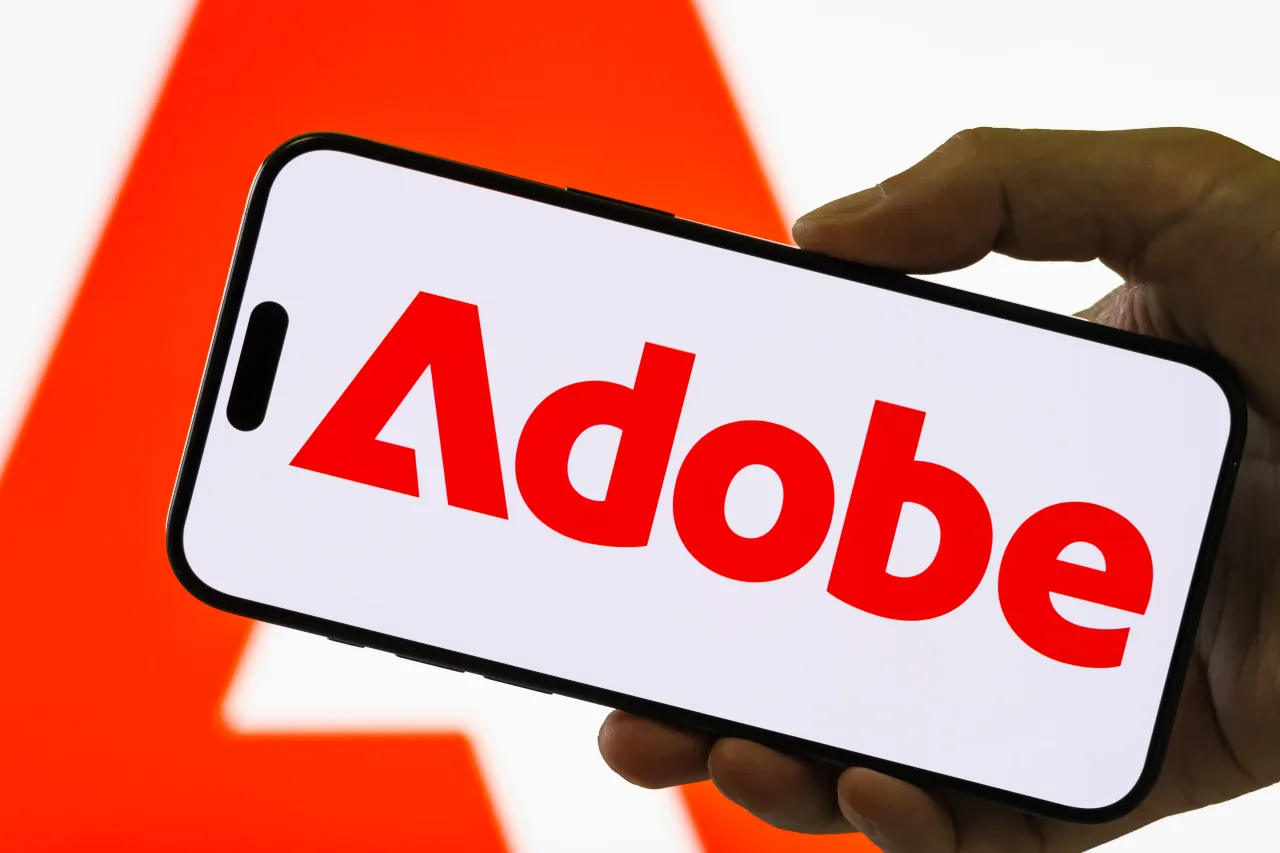 In this photo illustration, a smartphone held in a hand shows the logo of Adobe Inc. (NASDAQ: ADBE) on September 4, 2025 in Chongqing, China. 