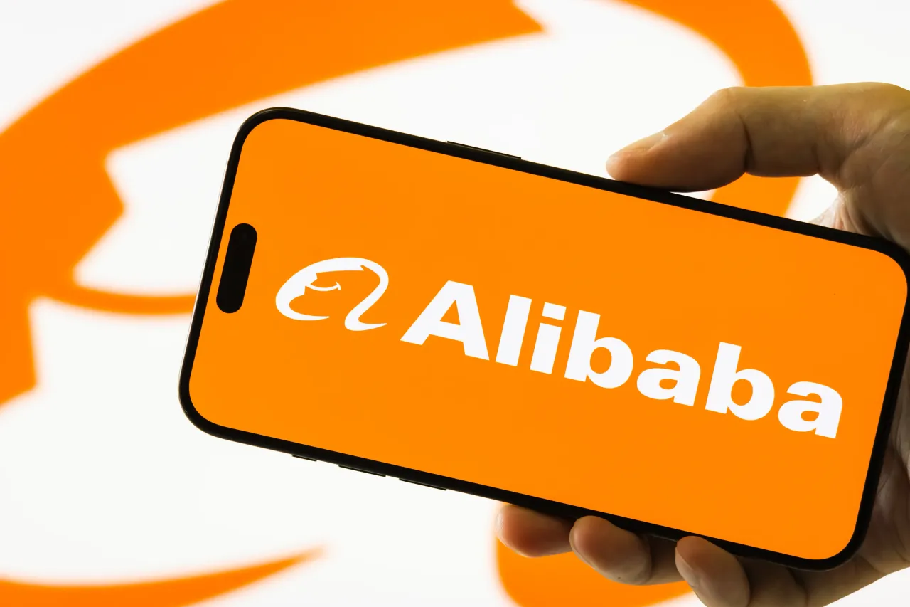 In this photo illustration, a person holds a smartphone displaying the logo of Alibaba Group Holding Limited (NYSE: BABA; HKEX: 9988), on August 26, 2025, in Chongqing, China.