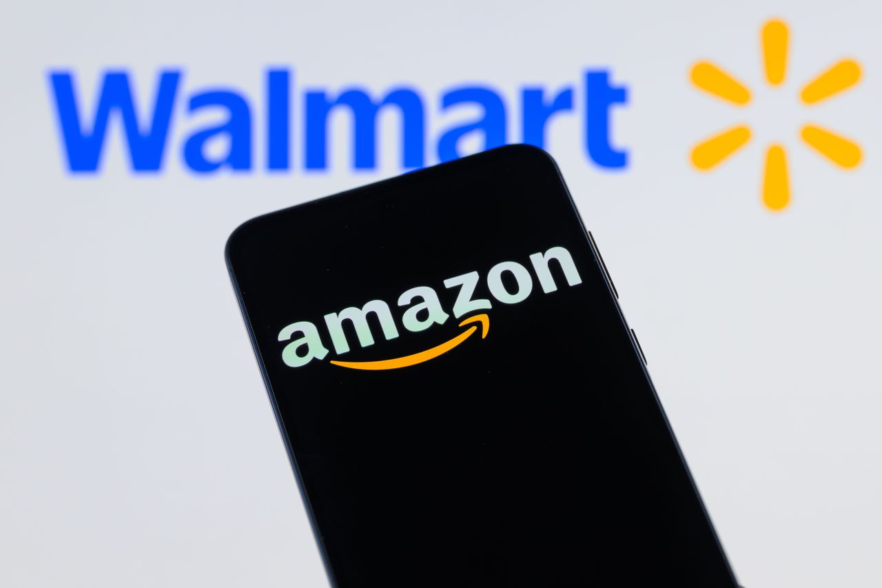 The Amazon logo is displayed on a mobile phone with the Walmart logo visible in the background. (Photo by Jonathan Raa/NurPhoto via Getty Images)