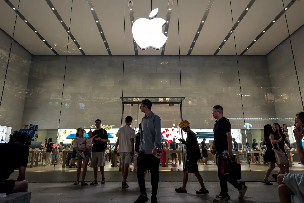  People walk past an Apple retail store under the illuminated logo of Apple Inc. (NASDAQ: AAPL) on August 29, 2025, in Chongqing, China. 