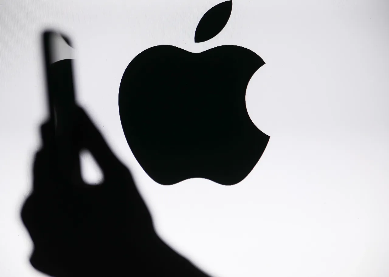 The Apple logo displays on a screen with a person holding a phone in Knurow, Poland, on September 20, 2025. 