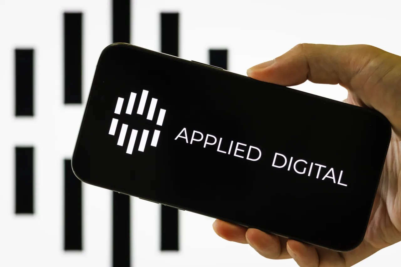 In this photo illustration, a hand holds a smartphone displaying the logo of Applied Digital Corporation with its brand logo seen in the background on September 28, 2025, in Chongqing, China. 