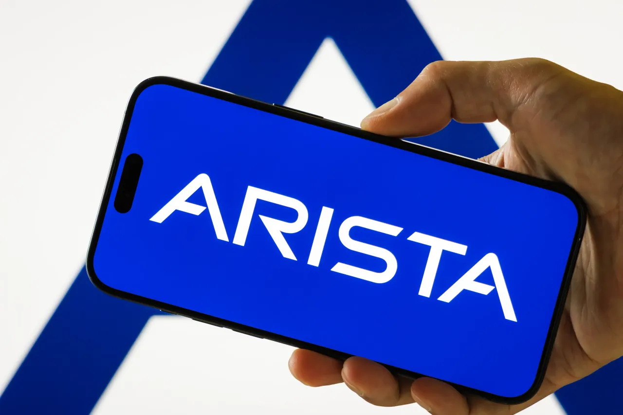 In this photo illustration, a person holds a smartphone displaying the logo of Arista Networks Inc. (NYSE: ANET) on July 31, 2025, in Chongqing, China. 