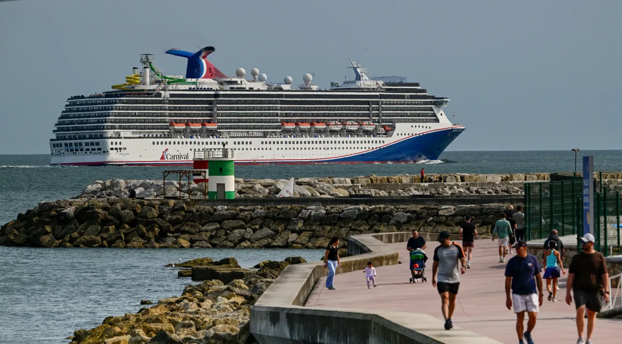 People are seen walking near the water as Carnival Miracle, a 88,500 GT Spirit-class cruise ship operated by Carnival Cruise Line, sails the Tagus River.