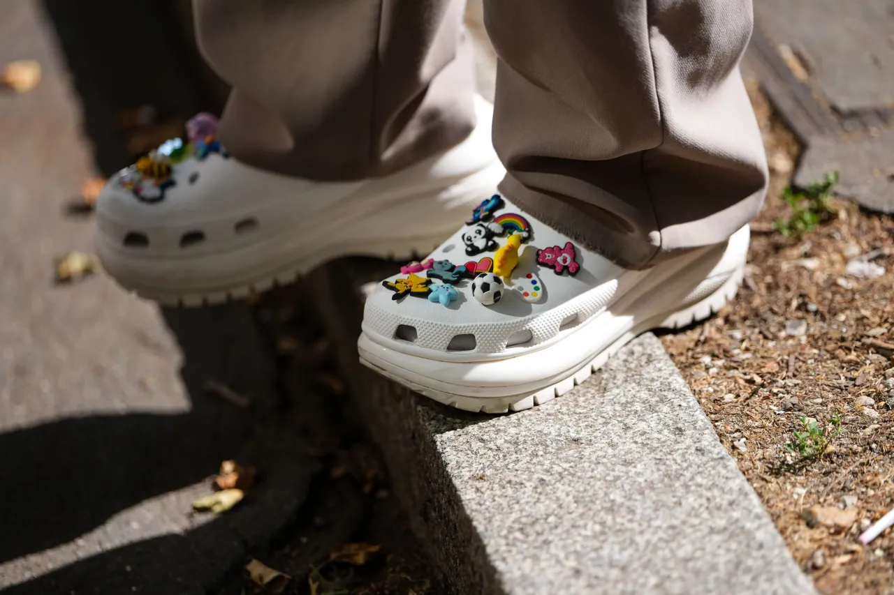 A guest wears white Crocs embellished with various colorful charms, including a panda, rainbow, soccer ball, and other playful designs, outside Egonlab, during Paris Fashion Week.