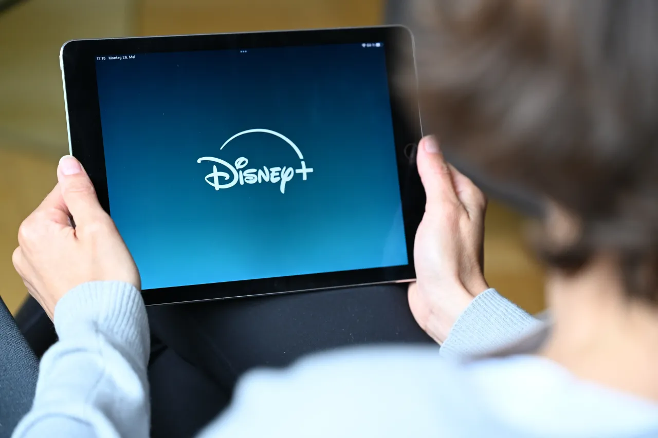 A woman looks at a tablet on which she has just opened the Disney+ streaming app (staged scene). 