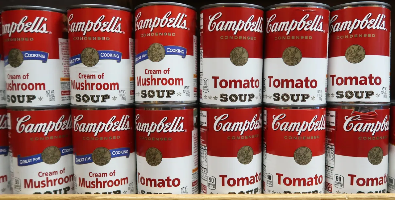 Cans of Campbell's soup sit on a shelf in a grocery store.