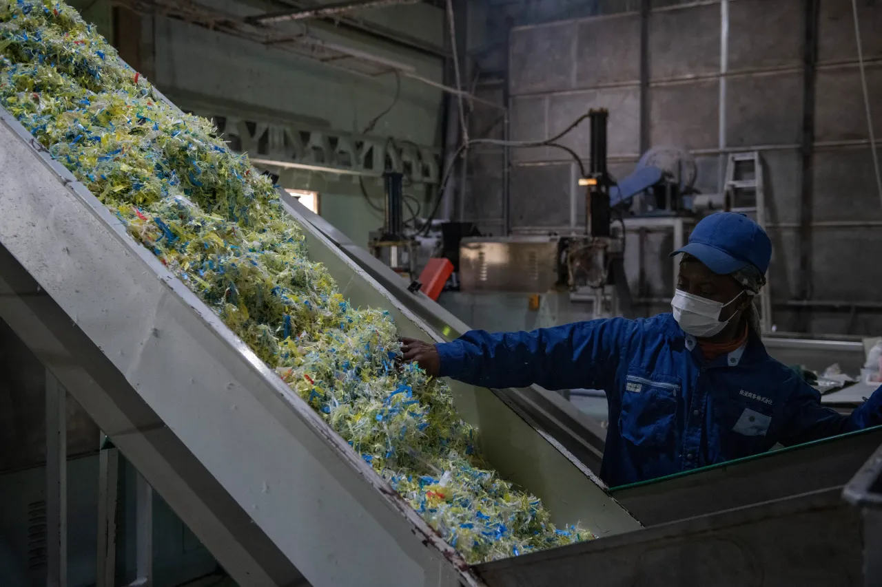 A worker checks shredded plastic as it passes along a conveyor belt during the recycling process.