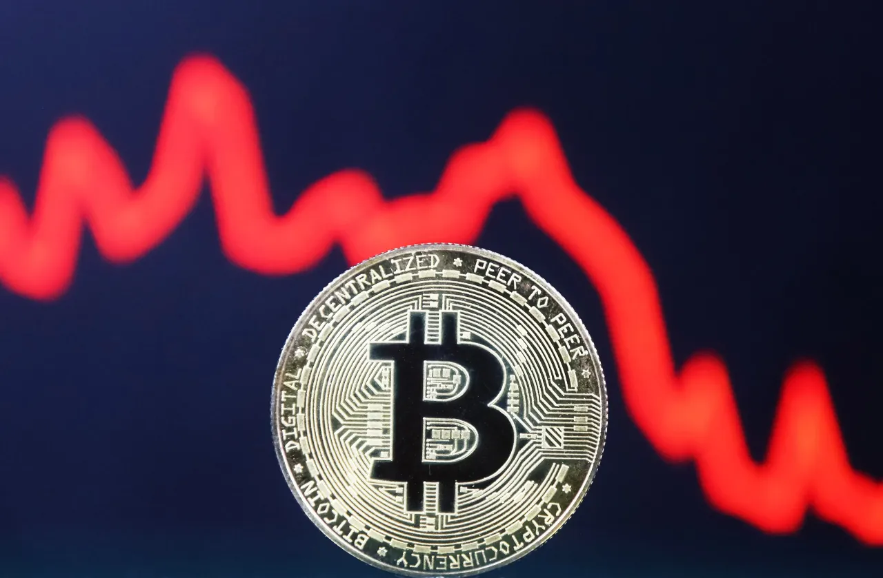 Bitcoin cryptocurrency coin and the red line of a graph are pictured in Kyiv on 29 July, 2021. (Photo by STR/NurPhoto via Getty Images)