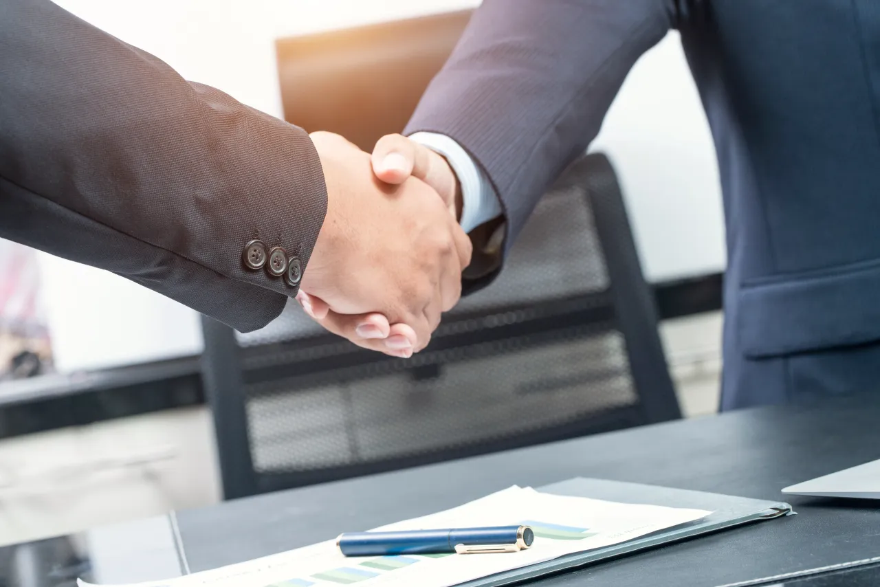 Close-up of two business people shaking hands while sitting at the working place. (Source: Getty Images)