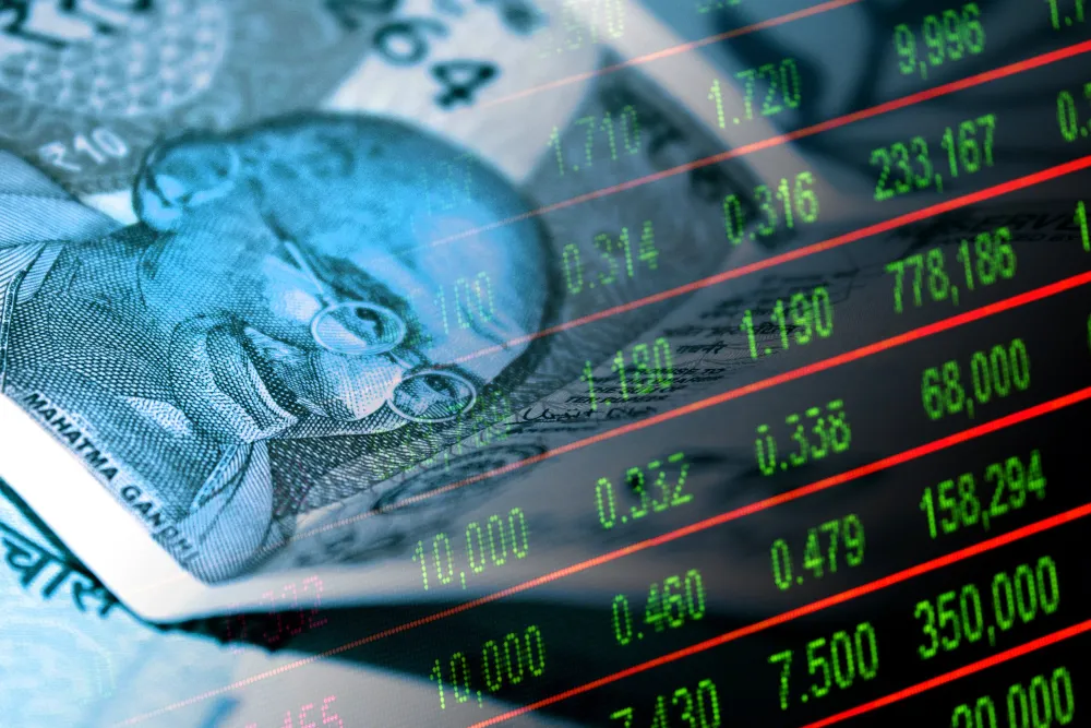 Indian rupee cash bills and stock market indicator board. | Image source: Getty Images