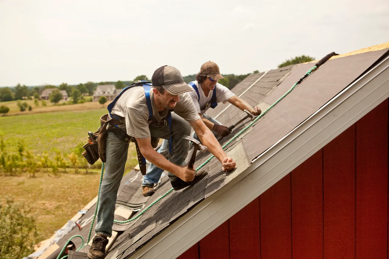 A team of men install watreproofing material and shingles to create a new roof on a rural building. (Source: GettyImages)