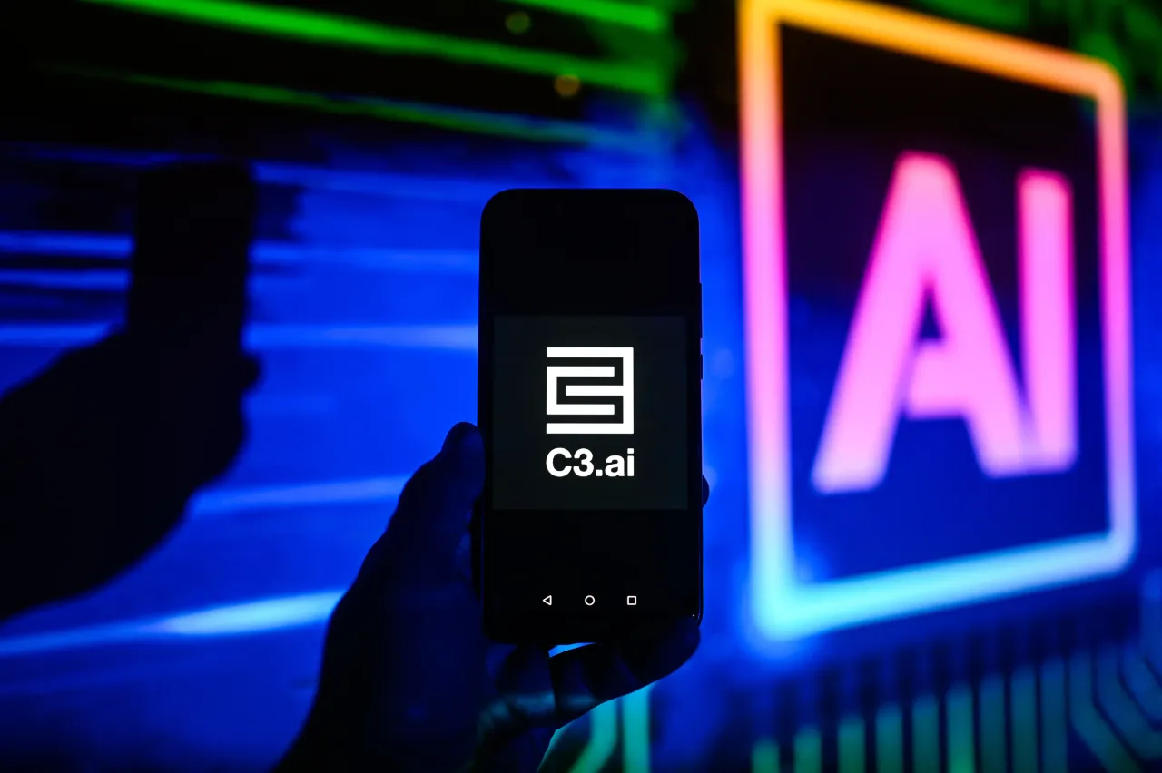 In this photo illustration a C3.ai logo is displayed on a smartphone with Artificial Intelligence symbol in the background. 