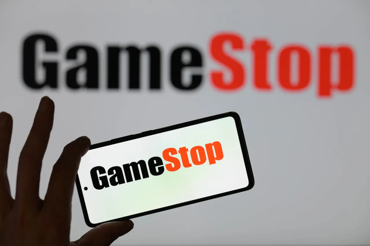 The GameStop logo is being displayed on a smartphone with GameStop visible in the background. (Photo by Jonathan Raa/NurPhoto via Getty Images)