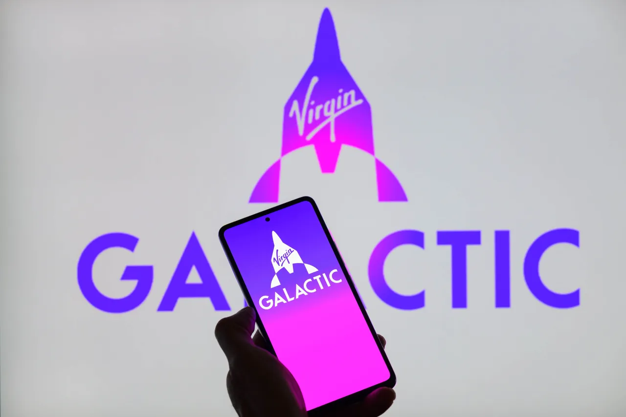 The Virgin Galactic logo is being displayed on a smartphone with Virgin Galactic Holdings visible in the background.