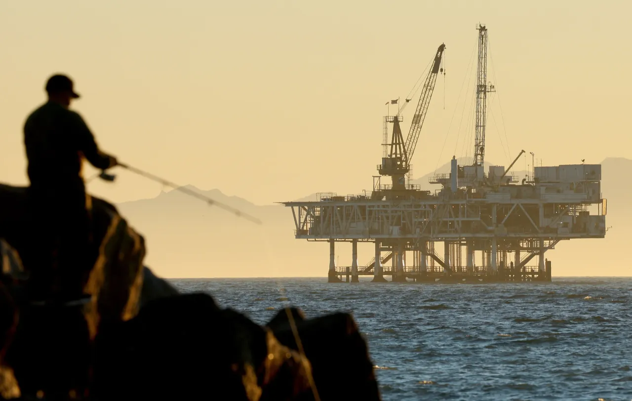A person fishes with offshore oil and gas platform Esther in the distance on January 5, 2025 in Seal Beach, California.