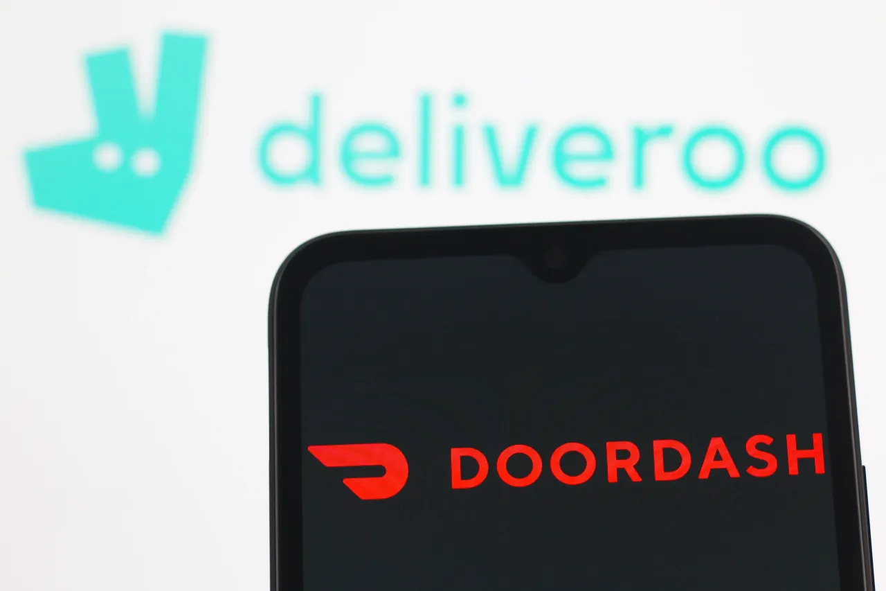 DoorDash logo is seen displayed on a smartphone screen and Deliveroo logo in the background. (Photo Illustration by Thomas Fuller/SOPA Images/LightRocket via Getty Images)