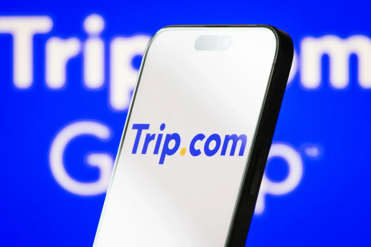 Trip.com logo is displayed on a smartphone screen, with the company's branding shown in the background. (Photo illustration by Cheng Xin/Getty Images)