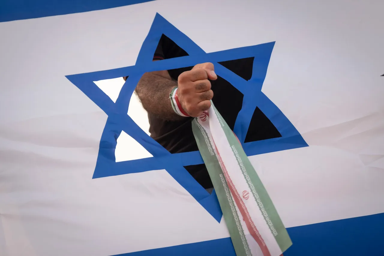 An Iranian man wearing his country's flag stands behind an anti-Israeli banner during a rall. (Photo by Morteza Nikoubazl/NurPhoto via Getty Images)