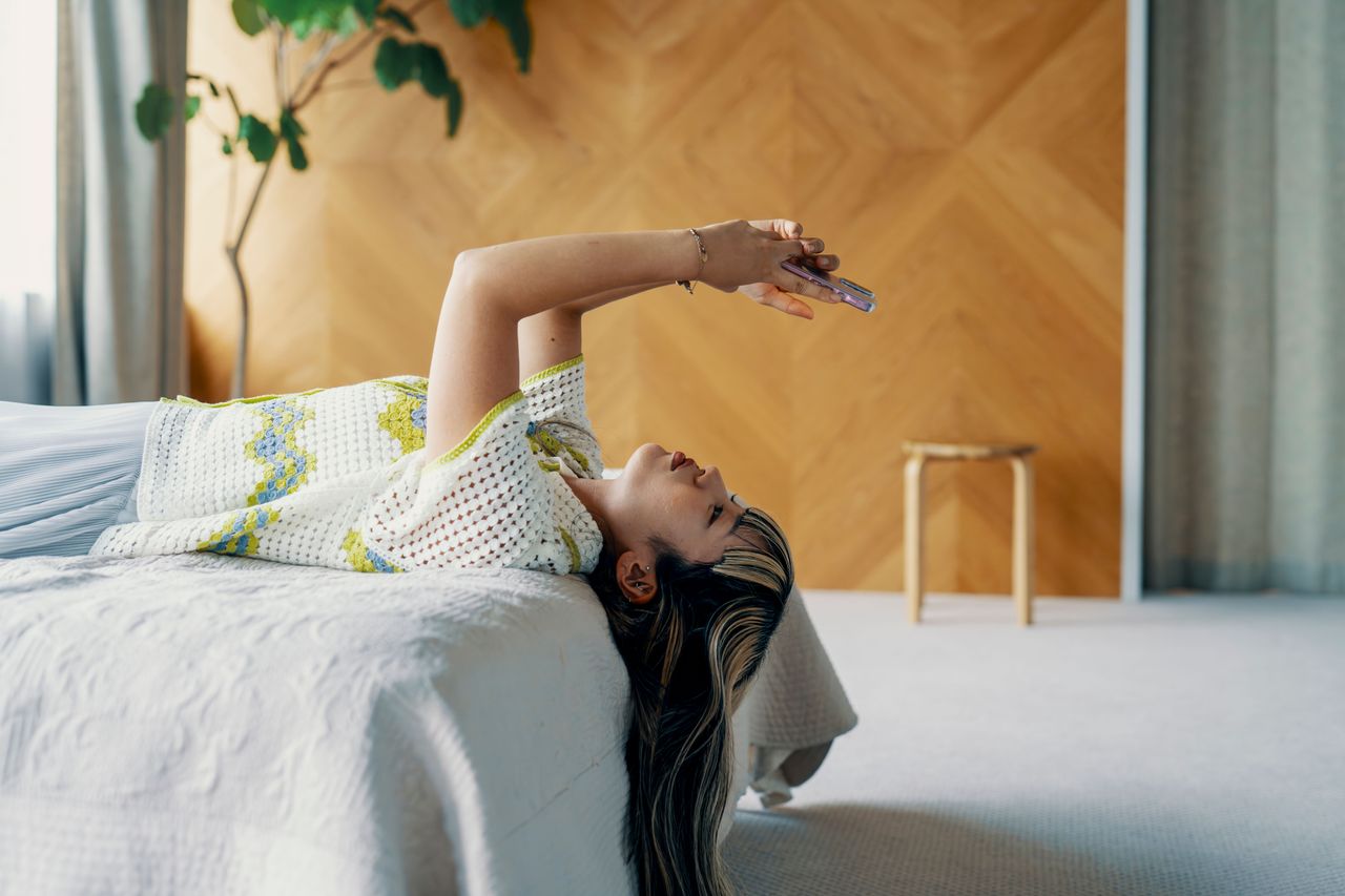 Woman lays on bed looking at her phone. Source: Getty Images