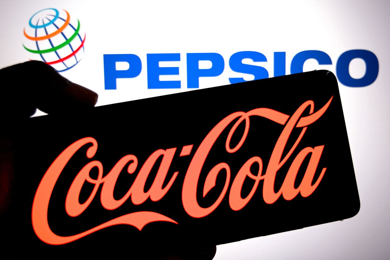 In this photo illustration, a Coca cola logo is seen displayed on a smartphone with a Pepsico logo in the background