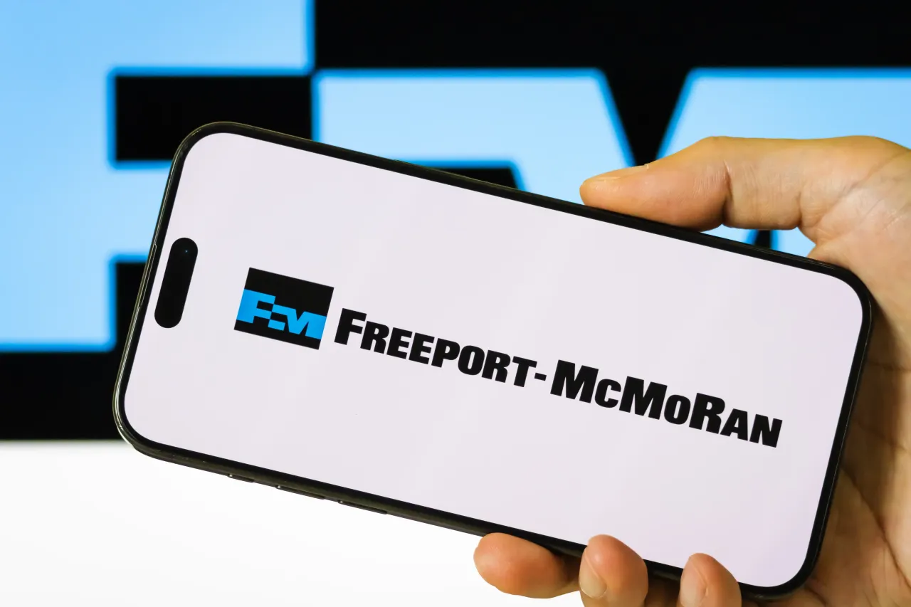 In this photo illustration, a person holds a smartphone displaying the logo of Freeport-McMoRan Inc. (NYSE: FCX).