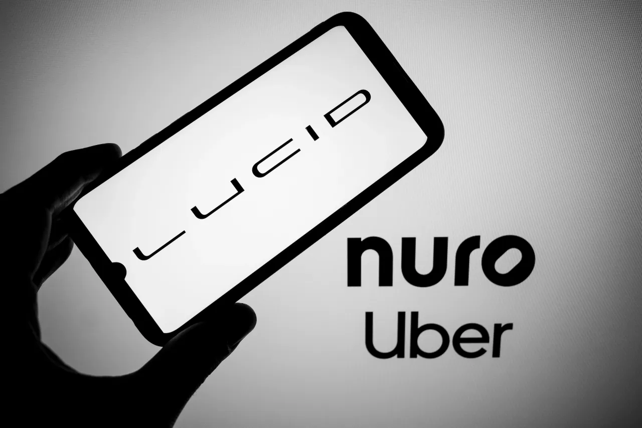 The Lucid logo appears on a smartphone screen, and the Nuro and Uber logos appear as the background on a laptop screen in this photo illustration in Athens, Greece, on August 17, 2025. (Photo by Nikolas Kokovlis/NurPhoto via Getty Images)