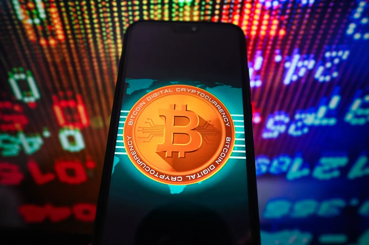 In this photo illustration, a Bitcoin logo is seen displayed on a smartphone with stock market percentages on the background.
