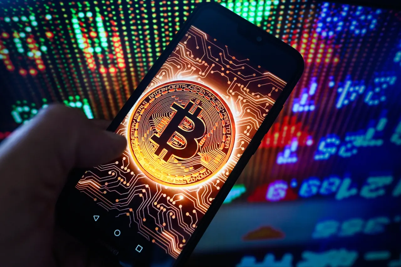 In this photo illustration, a Bitcoin logo is seen displayed on a smartphone with stock market percentages on the background.
