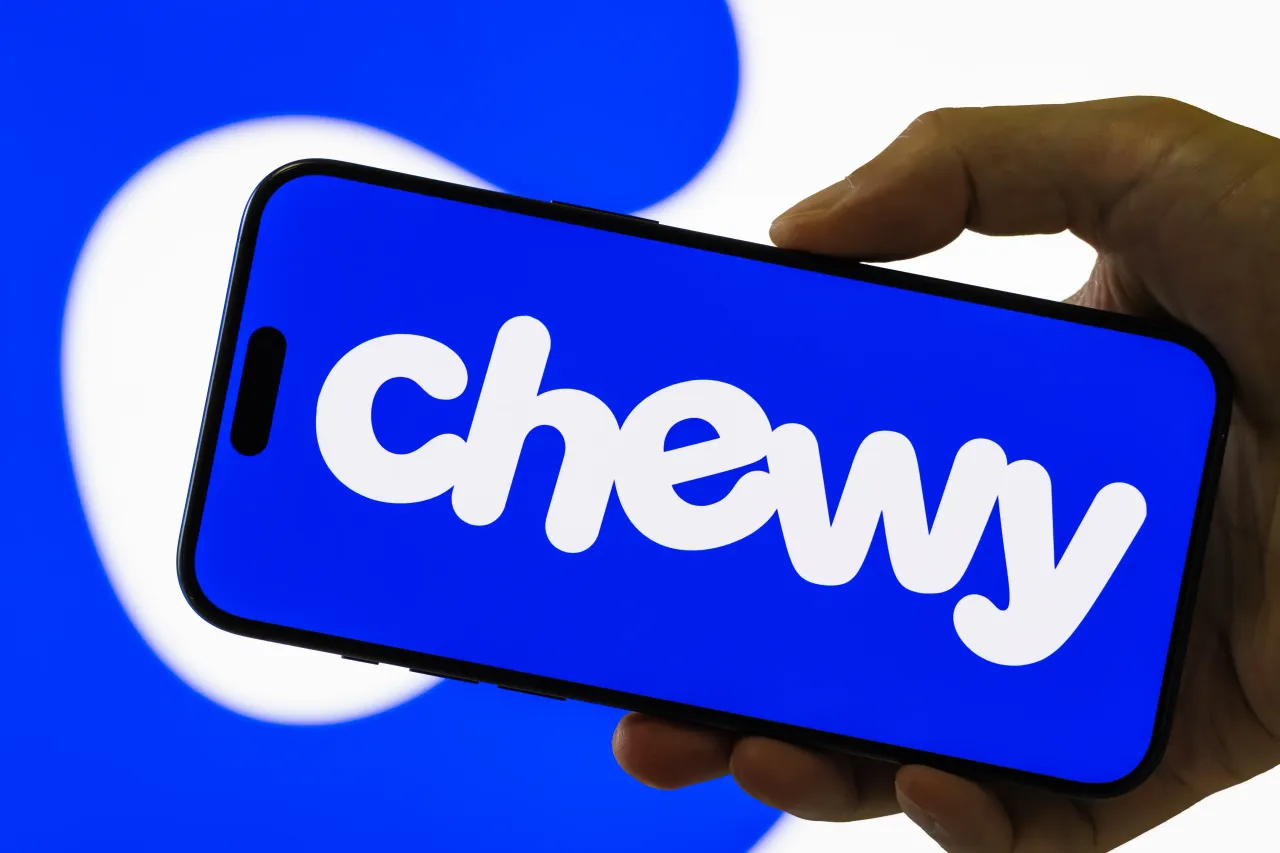 In this photo illustration, a smartphone held in a hand shows the logo of Chewy Inc. 