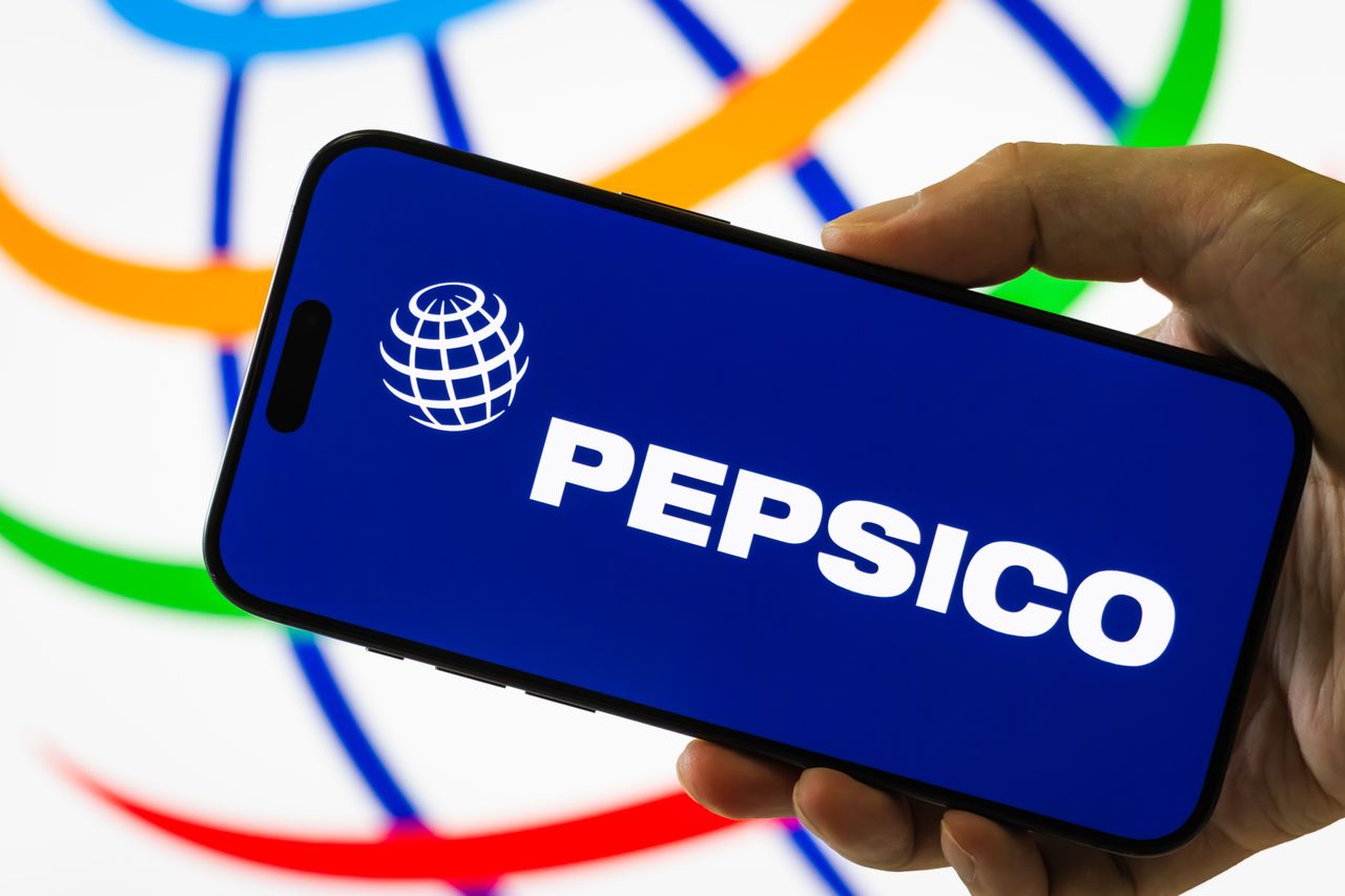 In this photo illustration, a hand holds a smartphone displaying the logo of PepsiCo, Inc.